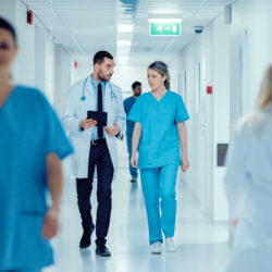 Surgeon and Female Doctor Walk Through Hospital Hallway, They Co